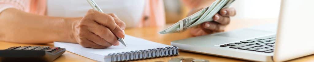 woman holding money while taking notes